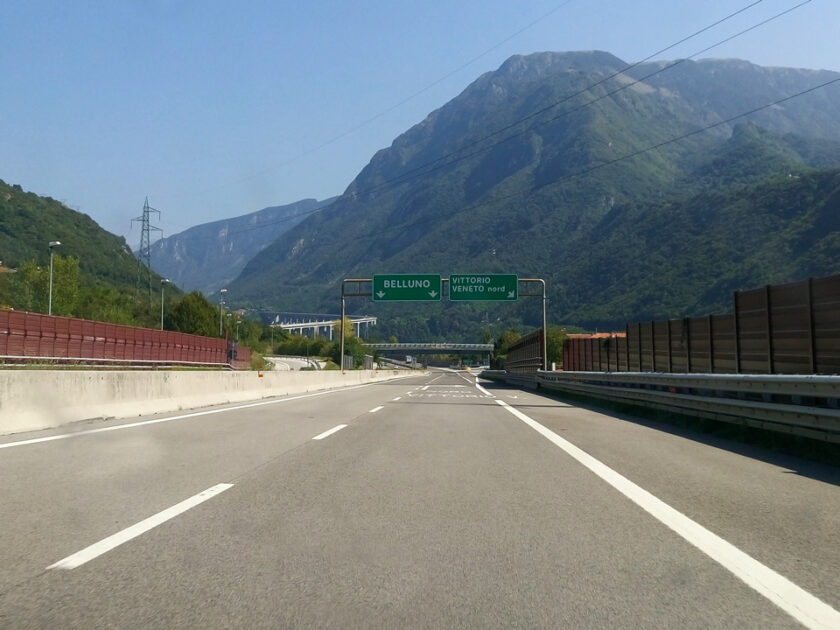 Conducir en Italia: reglas, consejos y trucos motorway Una autopista en Italia con señales verdes que indican Belluno y Vittorio Veneto y montañas al fondo
