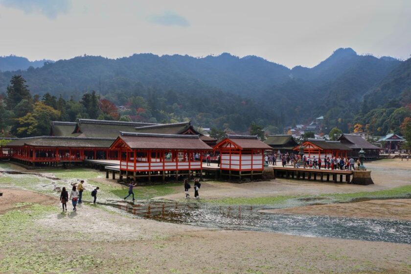 Japón en noviembre: itinerario de 10 días en fotos Miyajima before tide japan El santuario rojo brillante de Miyajima con la marea baja, con montañas cubiertas de follaje otoñal al fondo y el suelo cubierto de algas en primer plano